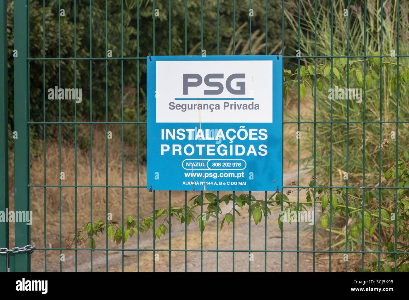 Close up view of a security sign indicating protected facilities on a green metal fence, with vegetation in the background, in portugal Stock Photo