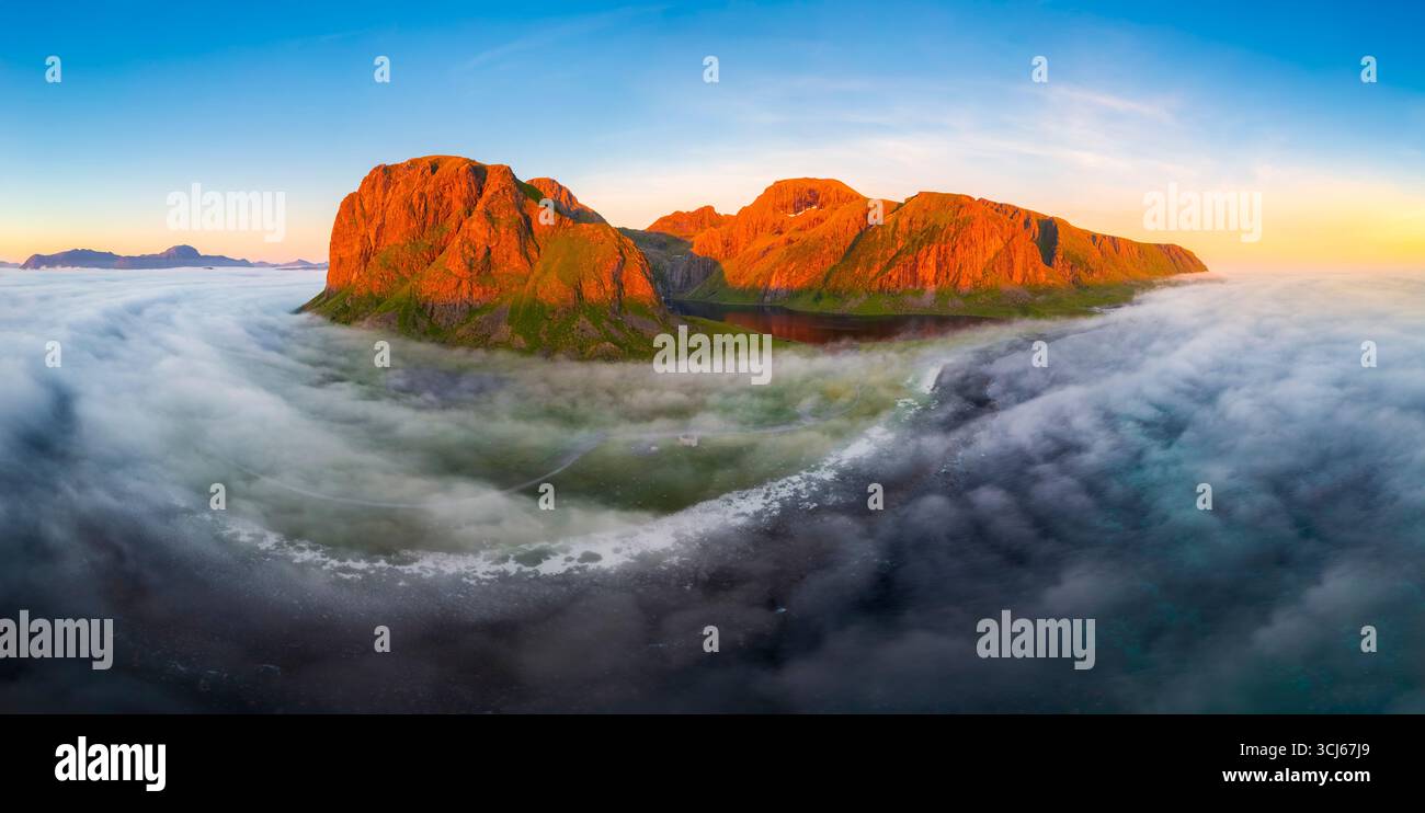 Aerial view of low clouds moving around the town of Eggum at midnight sun in summer. Eggum Unstad, Vestvagoy Lofoten, Islands, Norway, Europe. Stock Photo