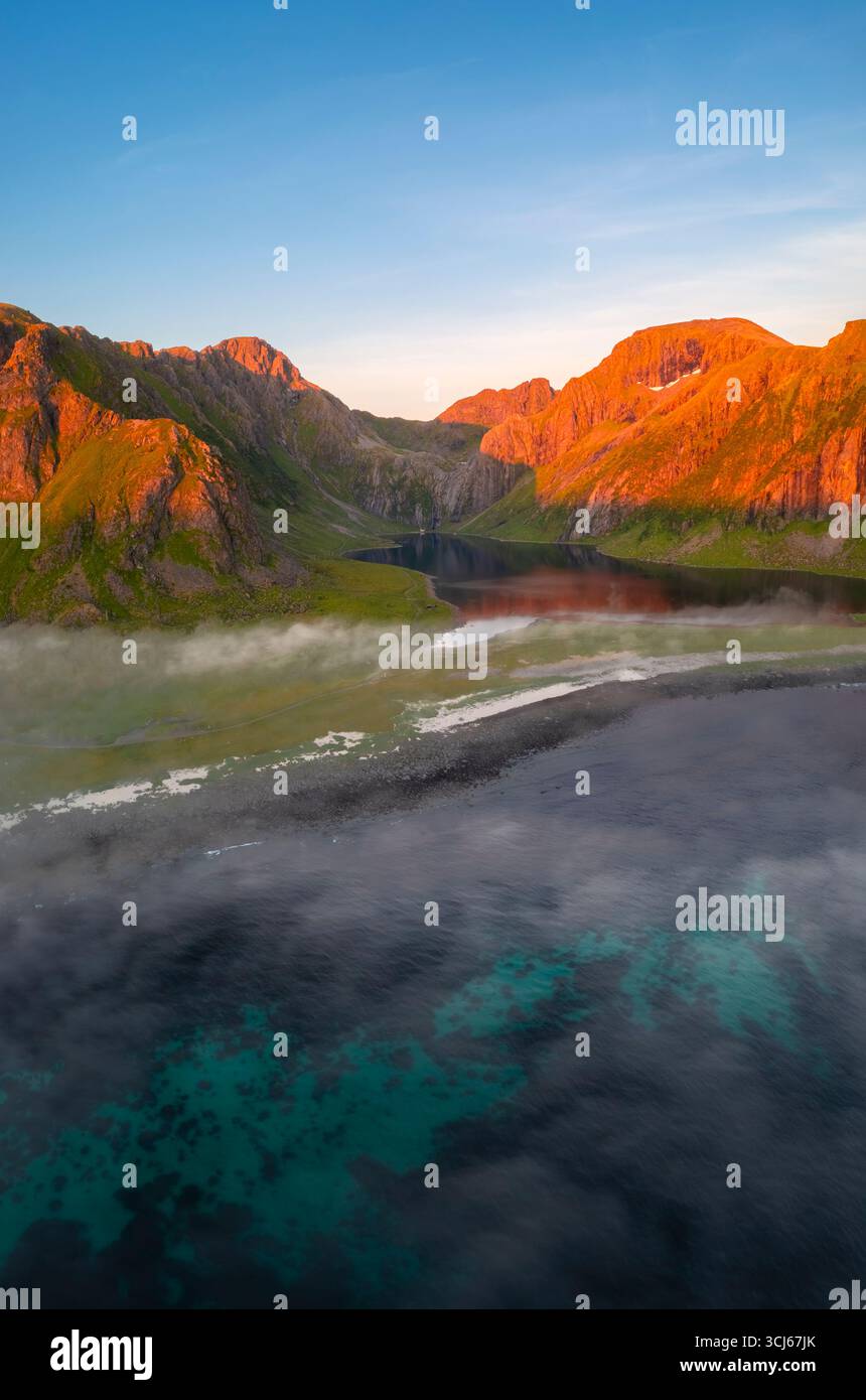 Aerial view of low clouds moving around the town of Eggum at midnight sun in summer. Eggum Unstad, Vestvagoy Lofoten, Islands, Norway, Europe. Stock Photo