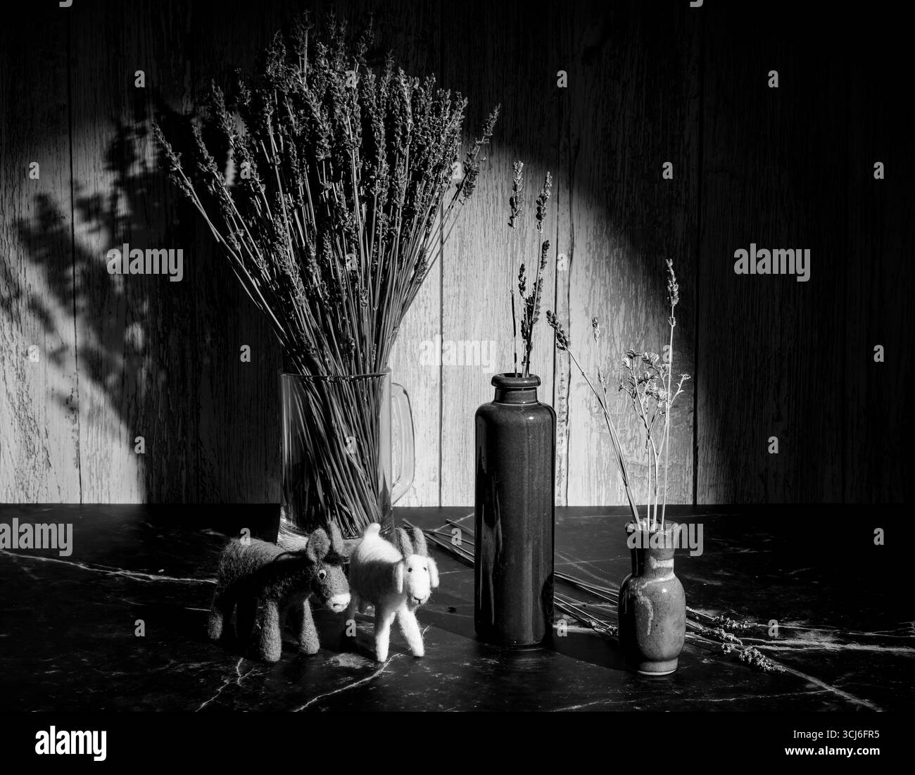 Felt toys of goats and donkeys, stems with lavender flowers in clay vases, in black and white Stock Photo