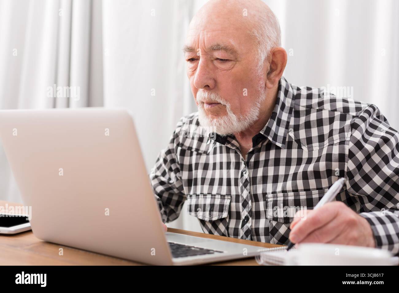 Mature man using laptop and writing in notepad Stock Photo
