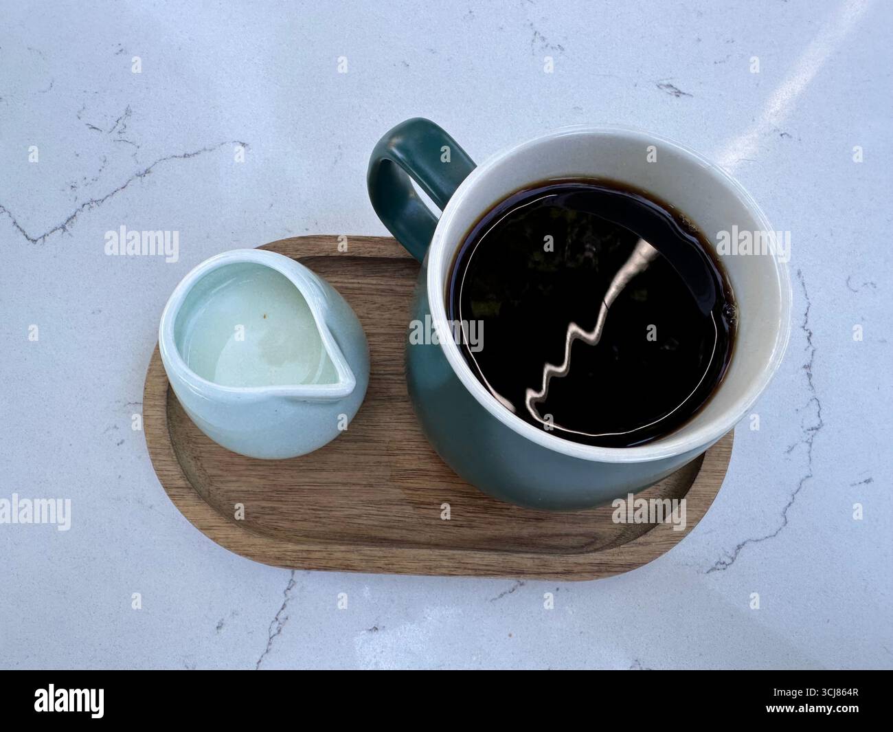 A cup of black coffee with a small jug of milk served on a wooden tray over marble surface. - Smartphone Captured Stock Image