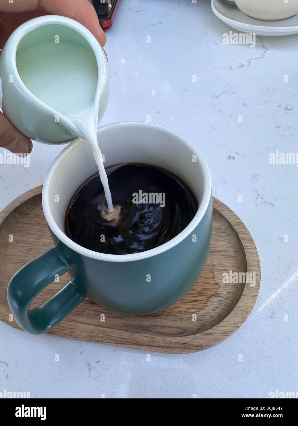 Close-up of milk being poured into a cup of black coffee placed on a wooden tray, lifestyle food and drink concept. - Smartphone Captured Stock Image