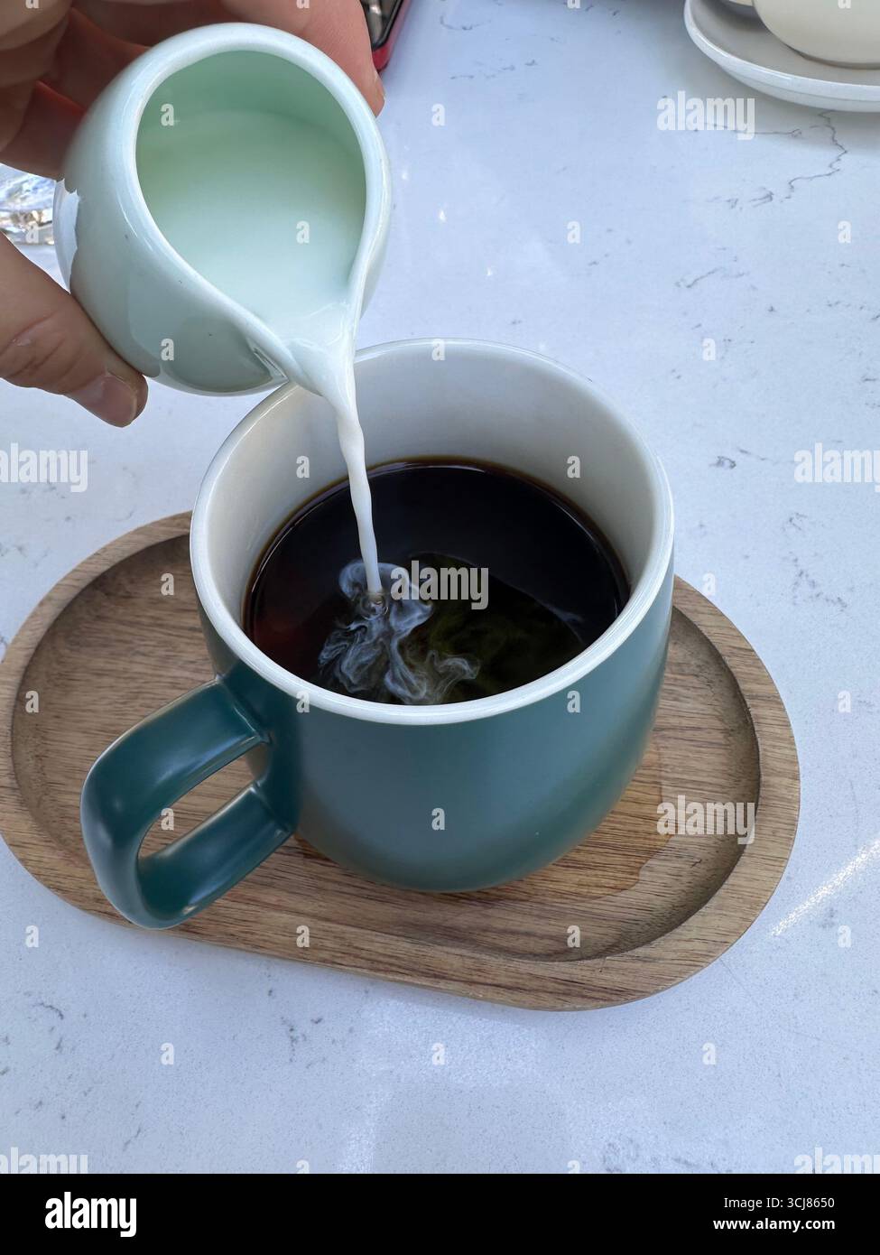 Close-up of milk being poured into a cup of black coffee placed on a wooden tray, lifestyle food and drink concept. - Smartphone Captured Stock Image