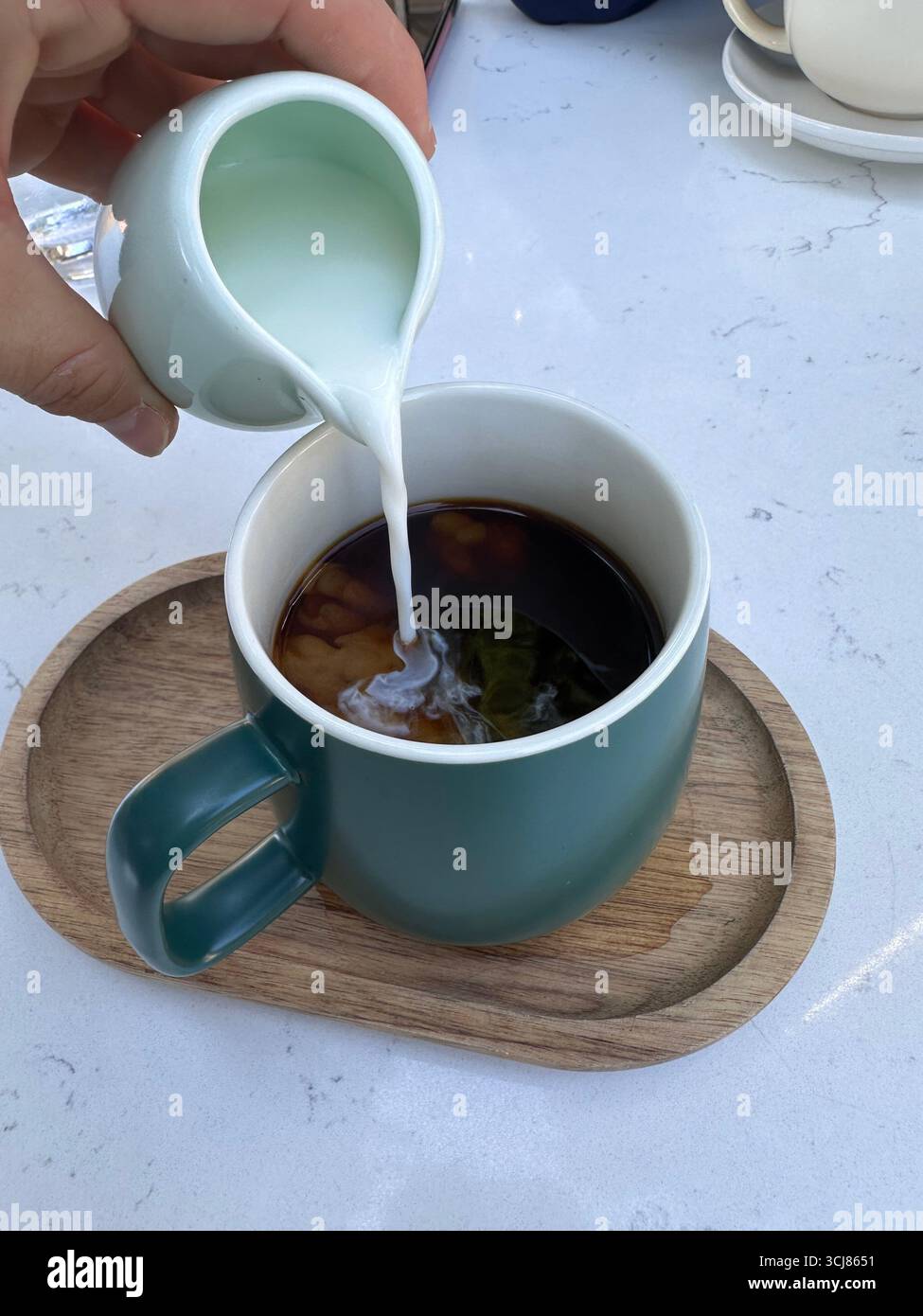 Close-up of milk being poured into a cup of black coffee placed on a wooden tray, lifestyle food and drink concept. - Smartphone Captured Stock Image