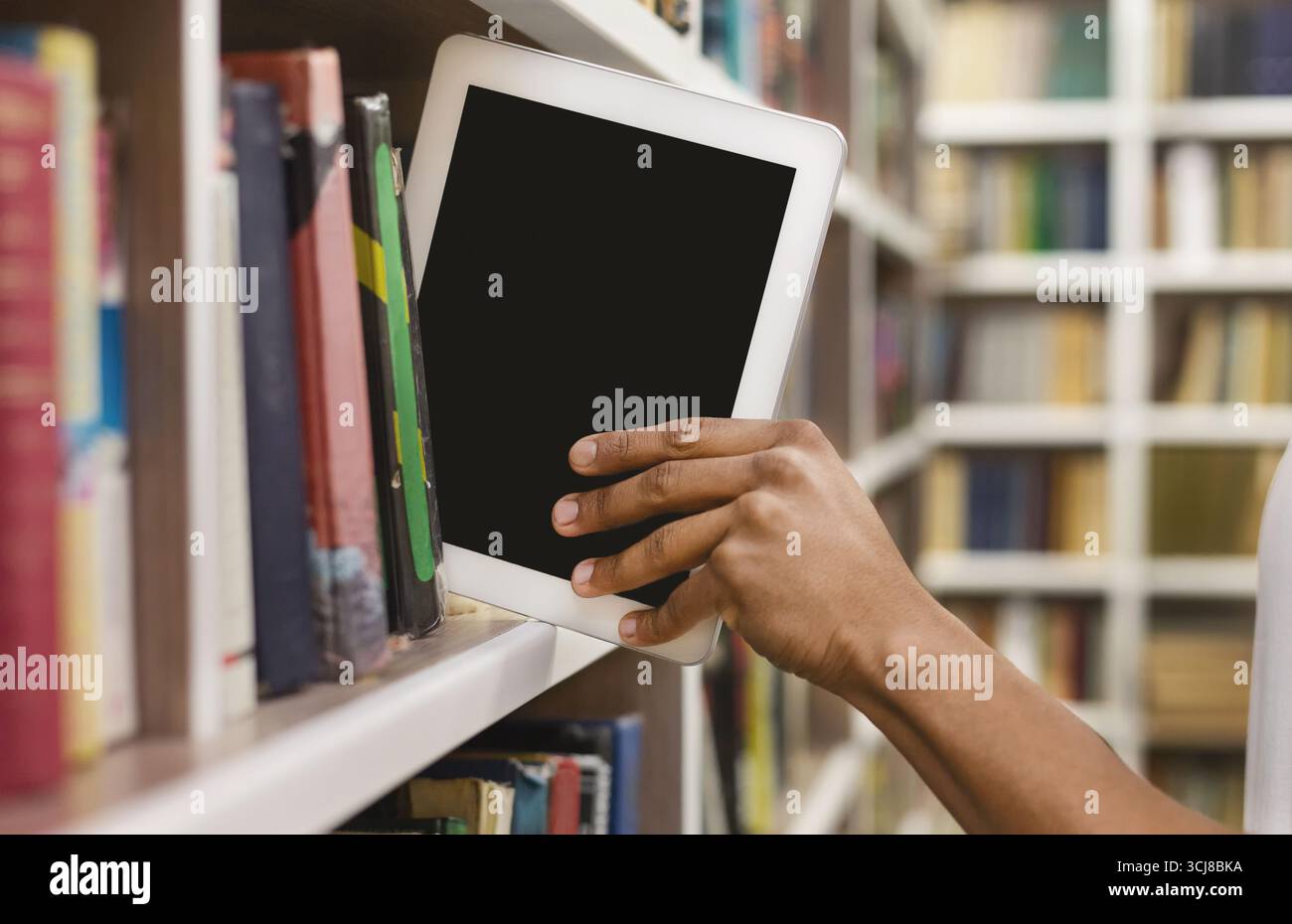 Afro student placing digital tablet on bookshelf Stock Photo
