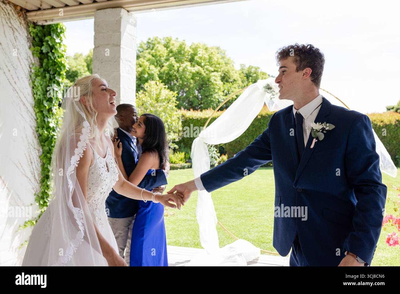Bride and groom joyfully dancing outdoors, celebrating wedding with friends Stock Photo