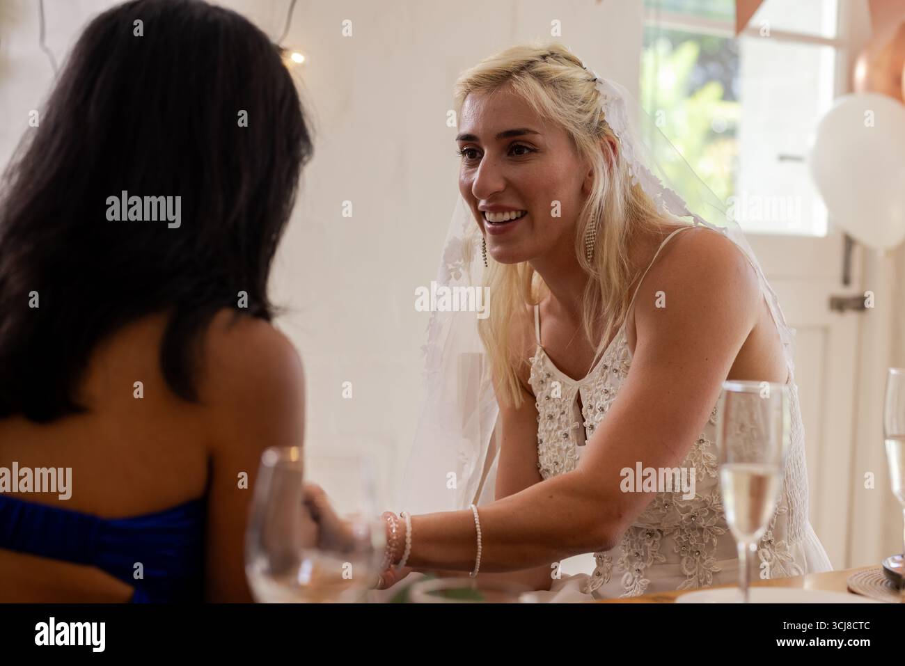 Bride in white dress joyfully chatting with guest at wedding reception Stock Photo