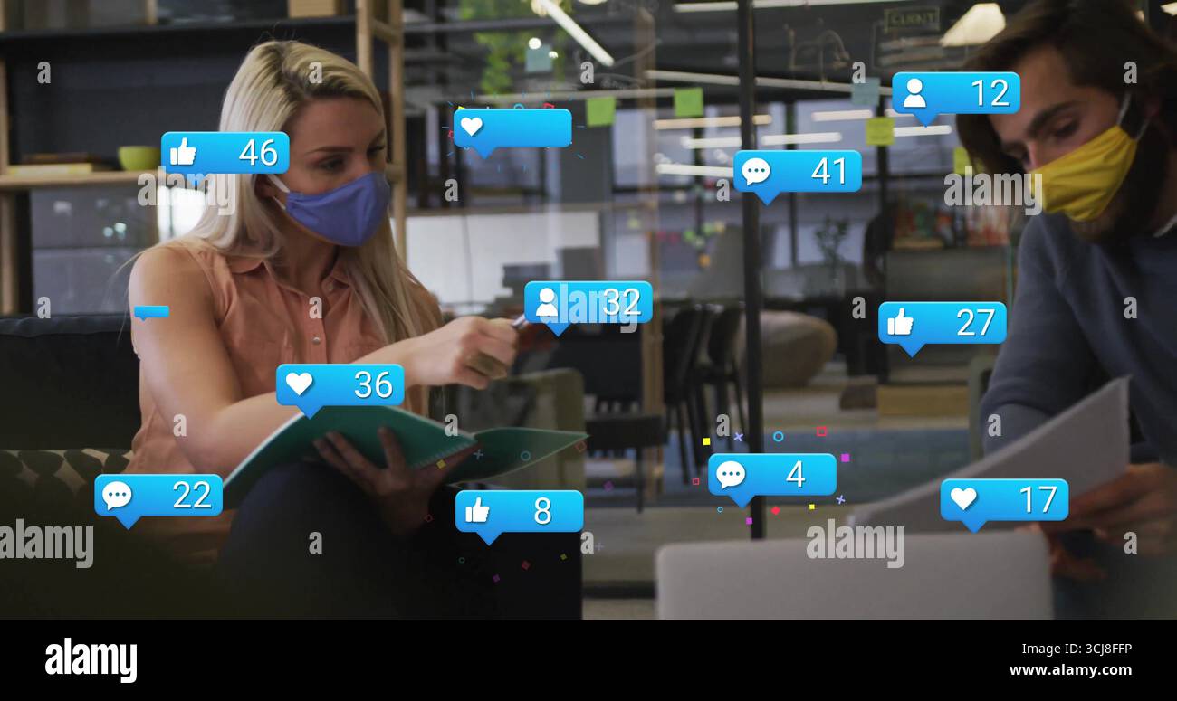 Two masked colleagues discussing binder in open-plan office, with floating icons and sticky notes Stock Photo