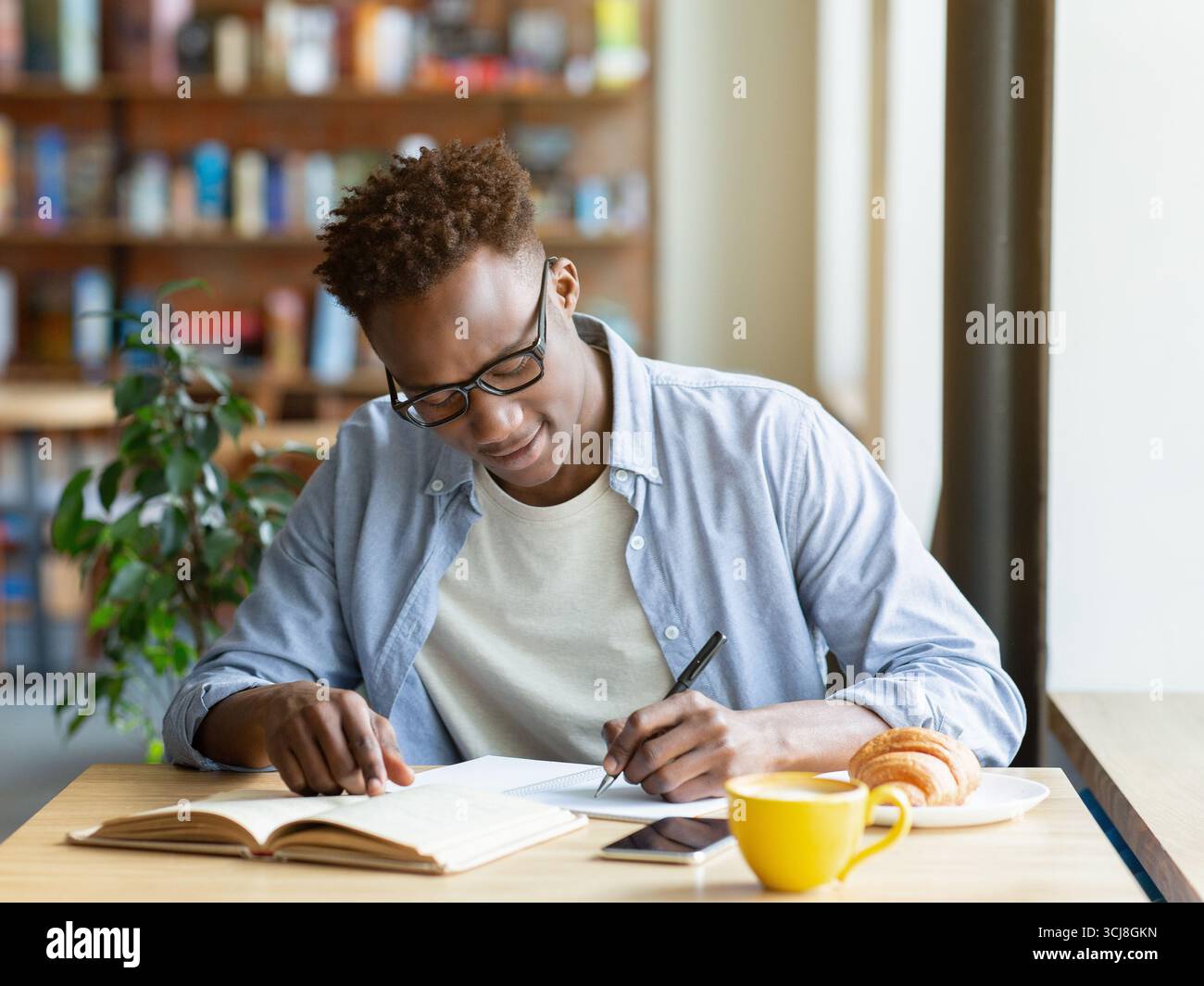 Hardworking black man writing down info from textbook, getting ready for test at cafe Stock Photo