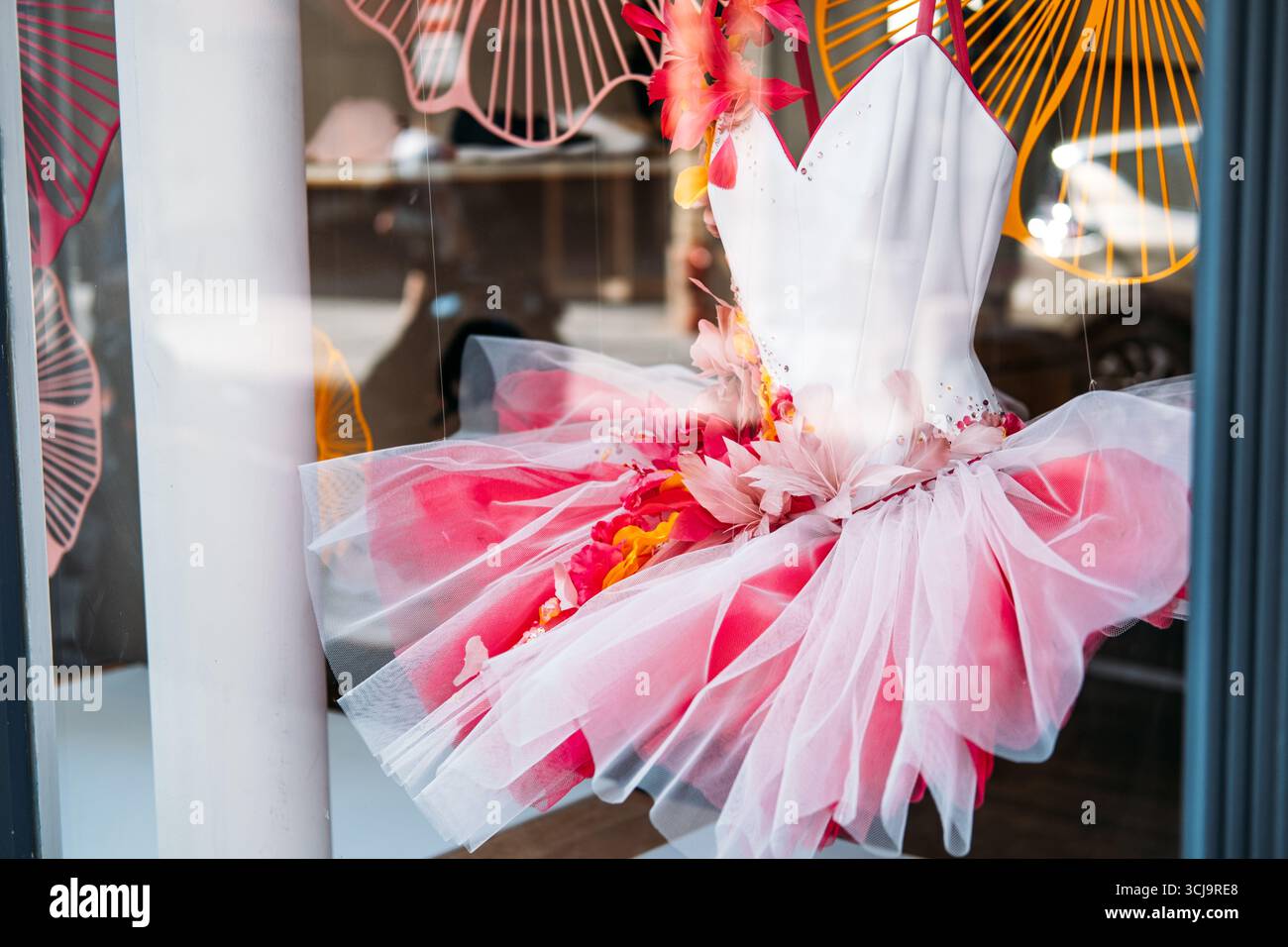 Pink and white ballerina tutu dress adorned with artificial flowers and tulle in a boutique display window. Costume craftsmanship, childhood fantasy Stock Photo