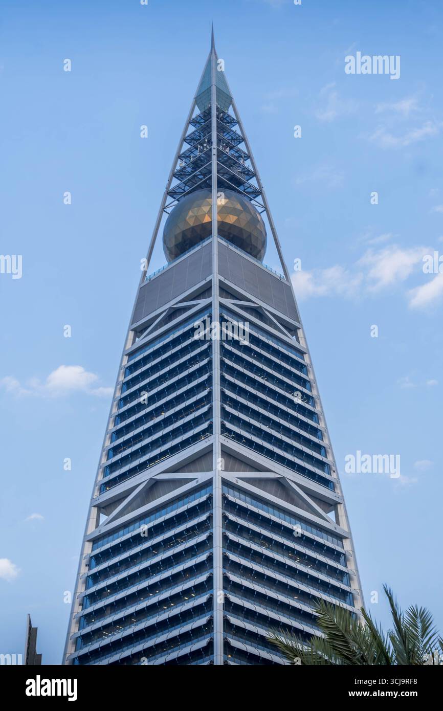 The Al Faisaliah Tower in Riyadh, Saudi Arabia, stands tall with its distinctive golden globe near the top, surrounded by palm trees, on a clear day. Stock Photo