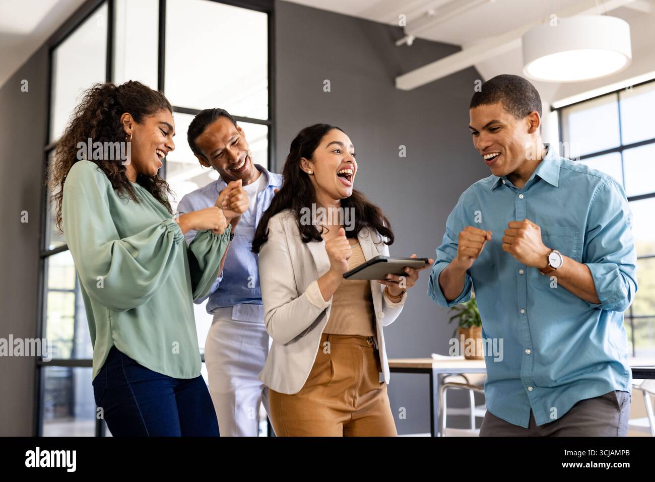 Diverse business team celebrating success with tablet in modern office Stock Photo
