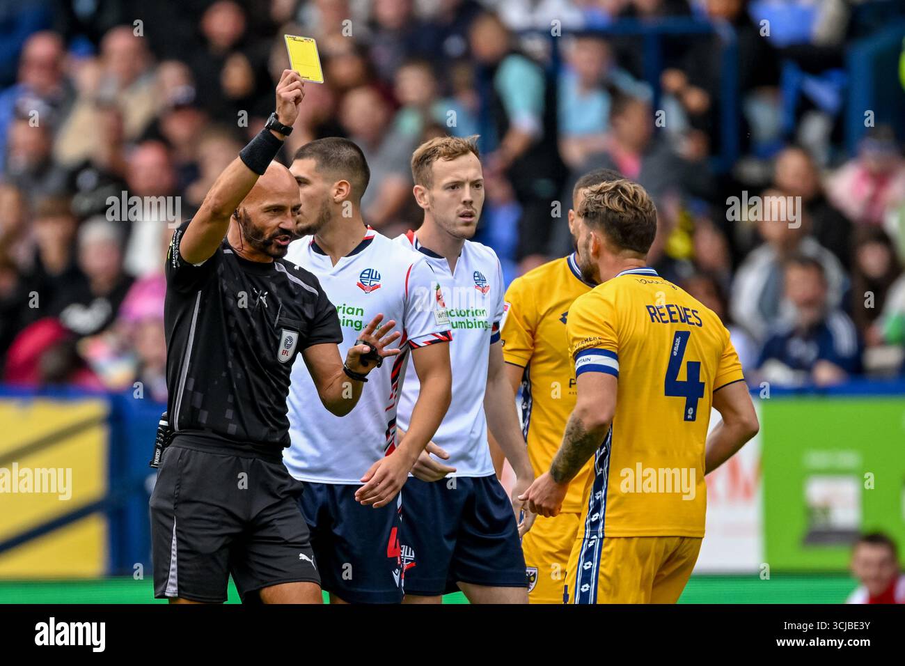 Referee Darren Drysdale books Jake Reeves of AFC Wimbledon during the ...