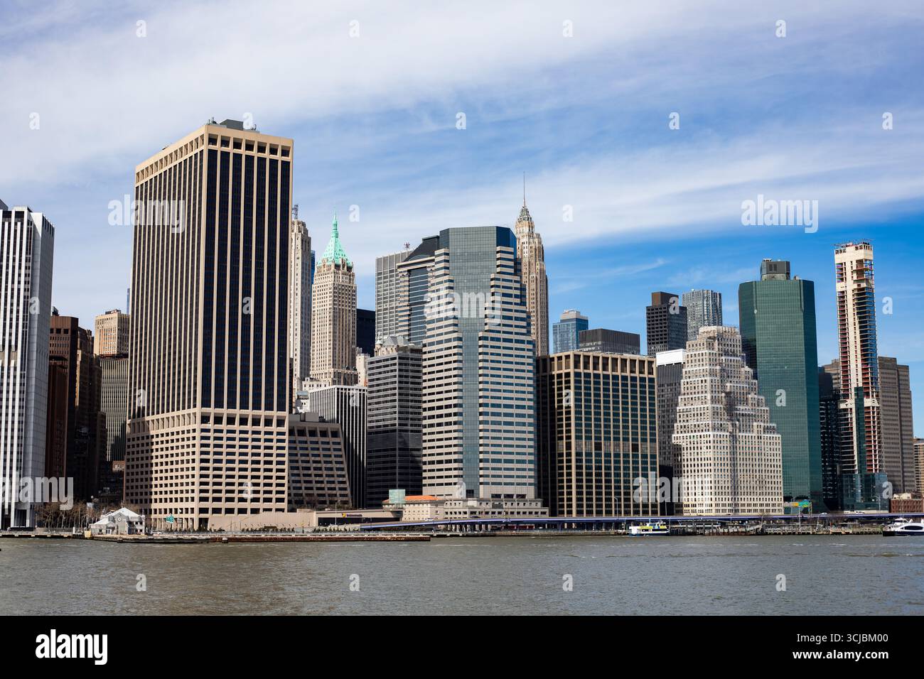 A panoramic view of New York City's Lower Manhattan skyline captured from across the harbor. The image features a mix of modern and historic skyscrape Stock Photo