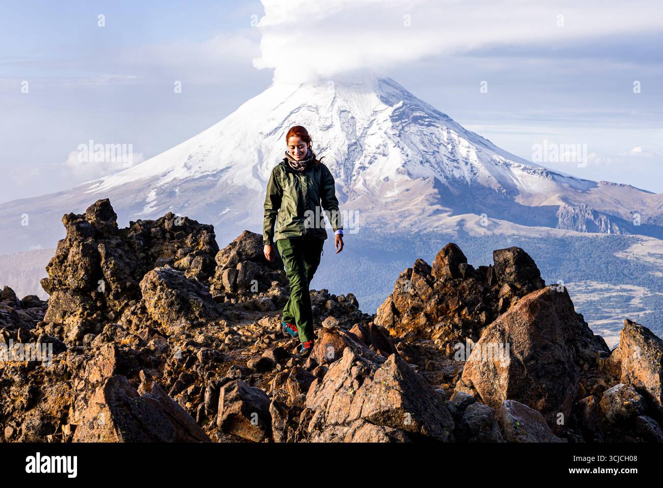 A hiker in a green jacket explores the rugged volcanic landscape of Iztaccihuatl, Mexico. The backdrop features stunning views of the snow-capped volc Stock Photo