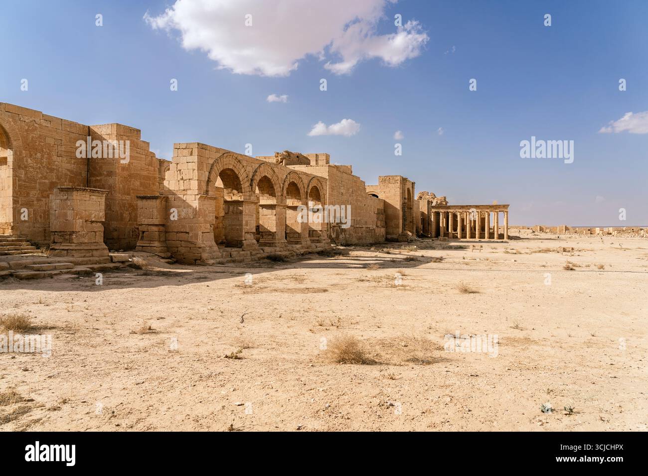 View of Hatra's main temple ruins in Iraq with stone arches and columns under a clear blue sky. The site reflects ancient Mesopotamian architecture an Stock Photo