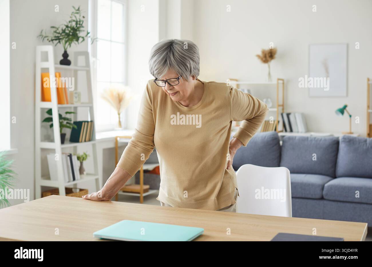 Senior woman standing at home touching her back suffering from backache. Stock Photo