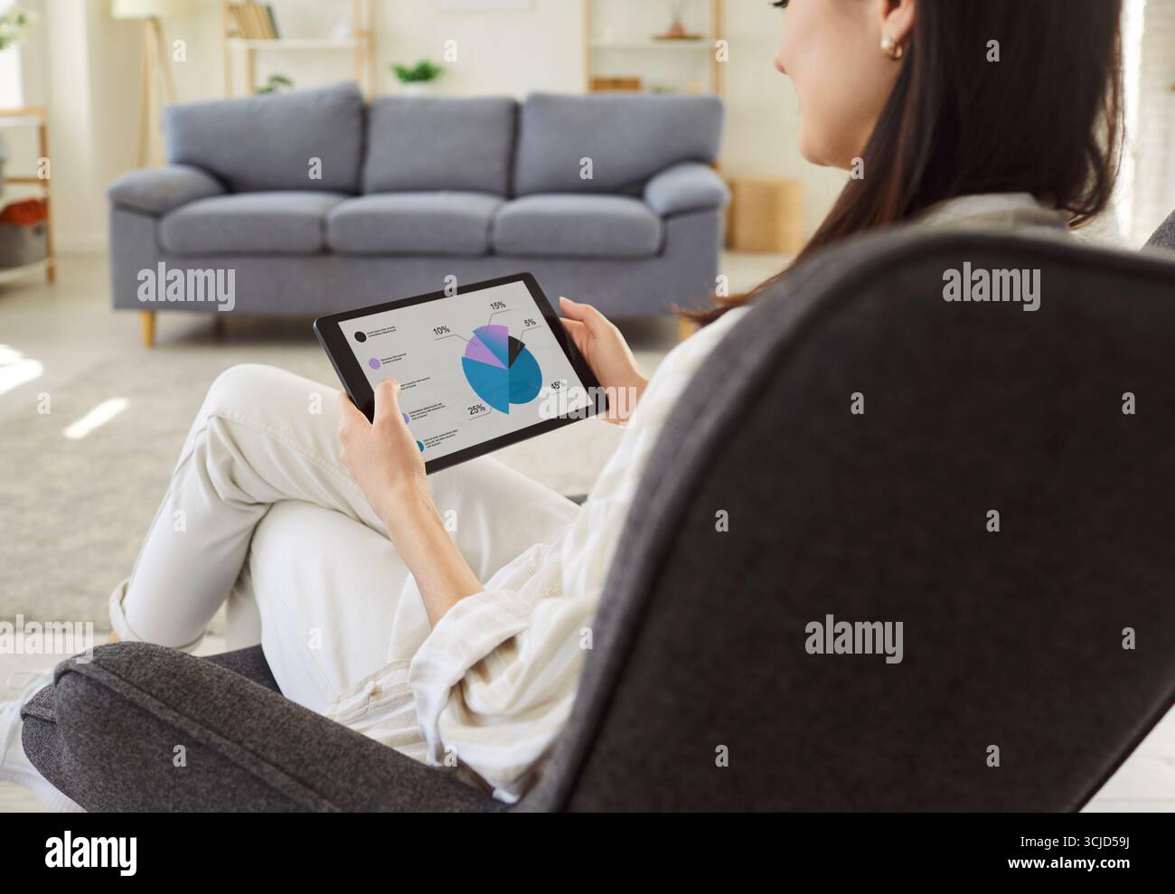 Young woman analyzing financial data at pie chart on tablet screen while working remotely from home. Stock Photo