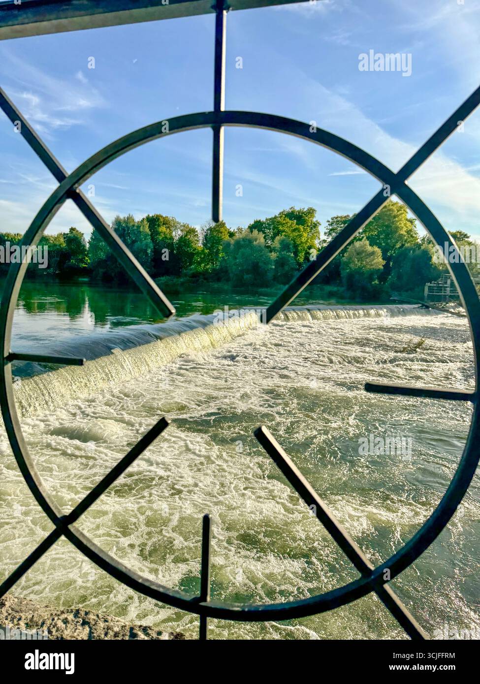 Scenic river with small dam and sacsading water, framed by circular metal structure under blue sky with clouds. - Smartphone Captured Stock Image