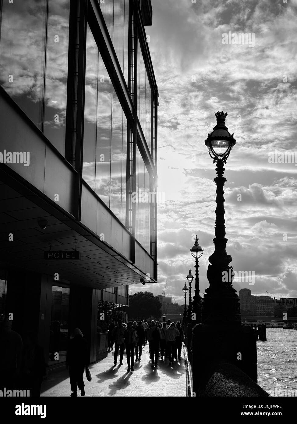 Lamps and pedestrians in silhouette against late afternoon sun on Thames South Bank, London - Smartphone Captured Stock Image