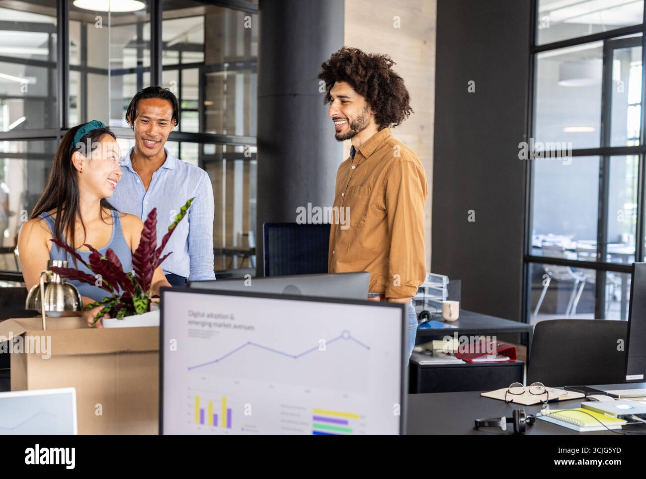 Discussing project with charts, diverse colleagues in modern office using computer Stock Photo