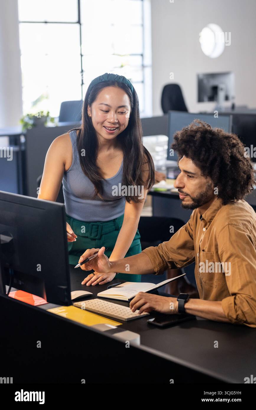 Colleagues collaborating at office desk, discussing project on computer screen Stock Photo