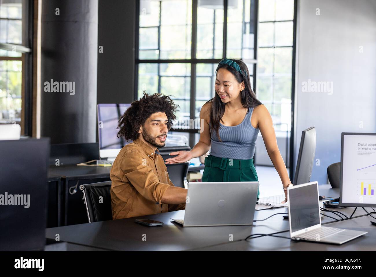 Colleagues collaborating on project using laptops in modern office setting Stock Photo