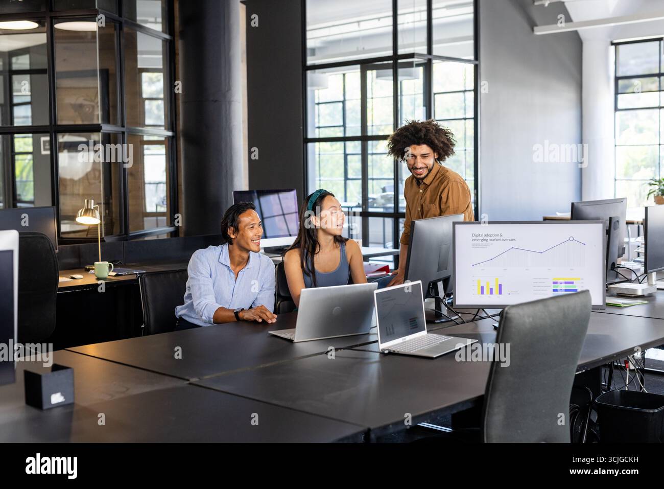 Collaborating in modern office, diverse team analyzing data on computer screens Stock Photo