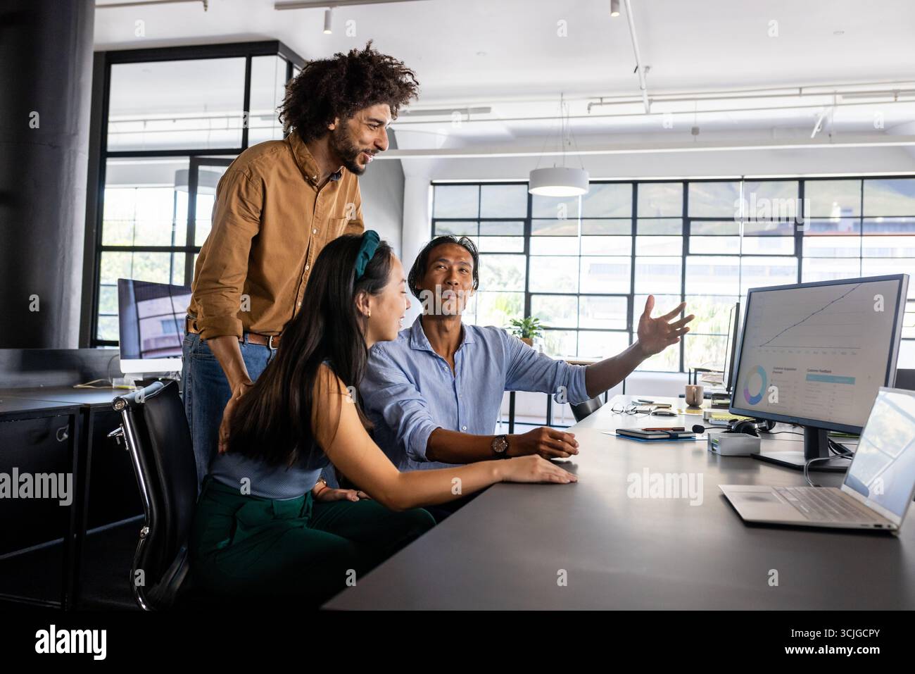 Diverse business team discussing project at office desk, analyzing data on computer Stock Photo