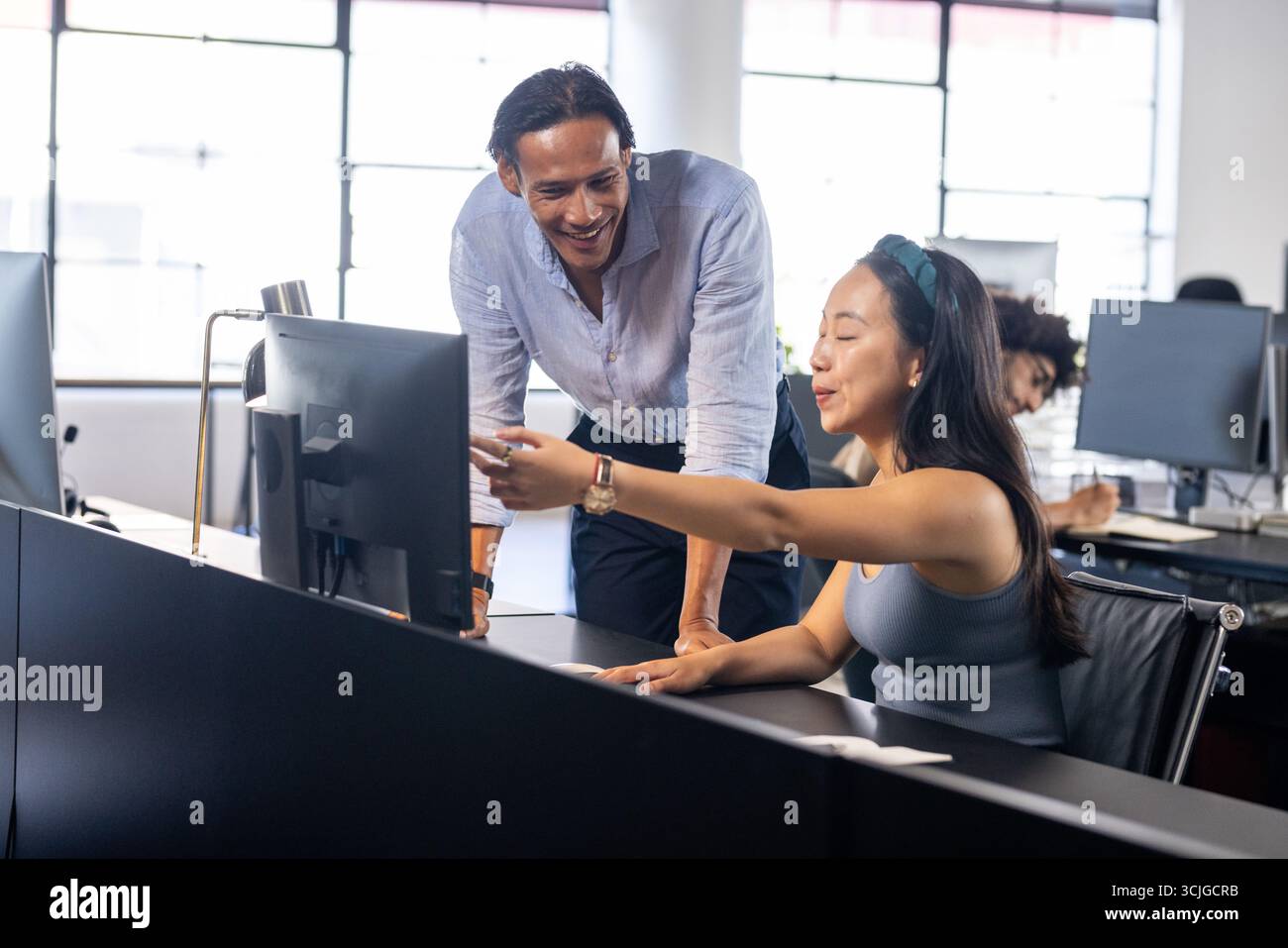 Colleagues collaborating at office desk, discussing project on computer screen Stock Photo