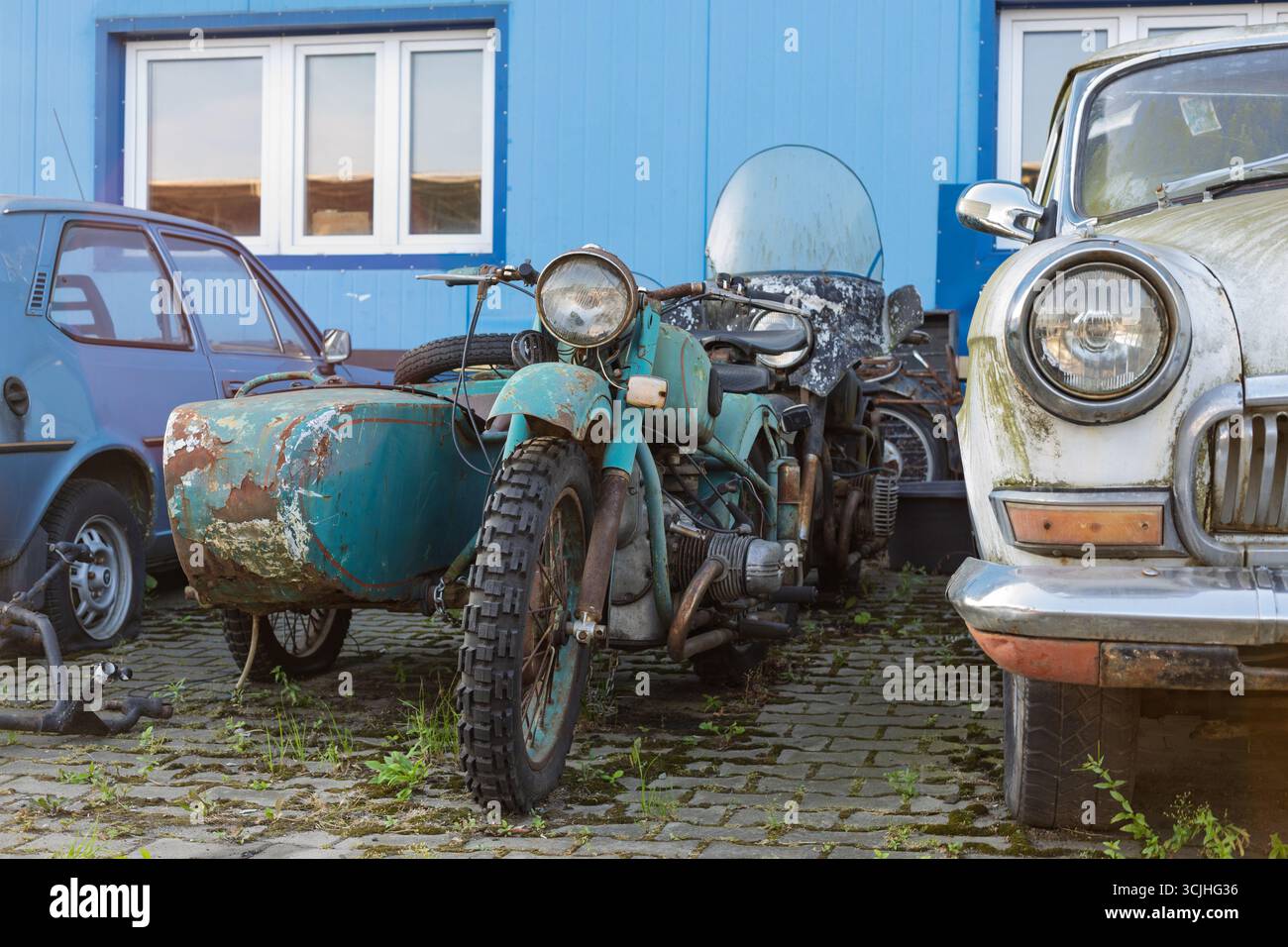 Wroclaw, Poland - August 28 2025: Rusted Soviet sidecar motorcycles next to mossy GAZ Volga Stock Photo