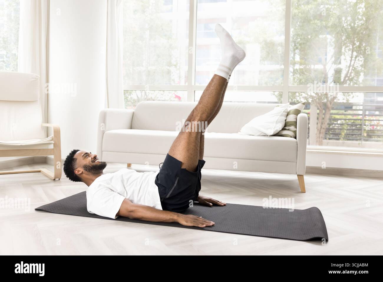 Smiling young man swing press on gymnastic mat at home Stock Photo