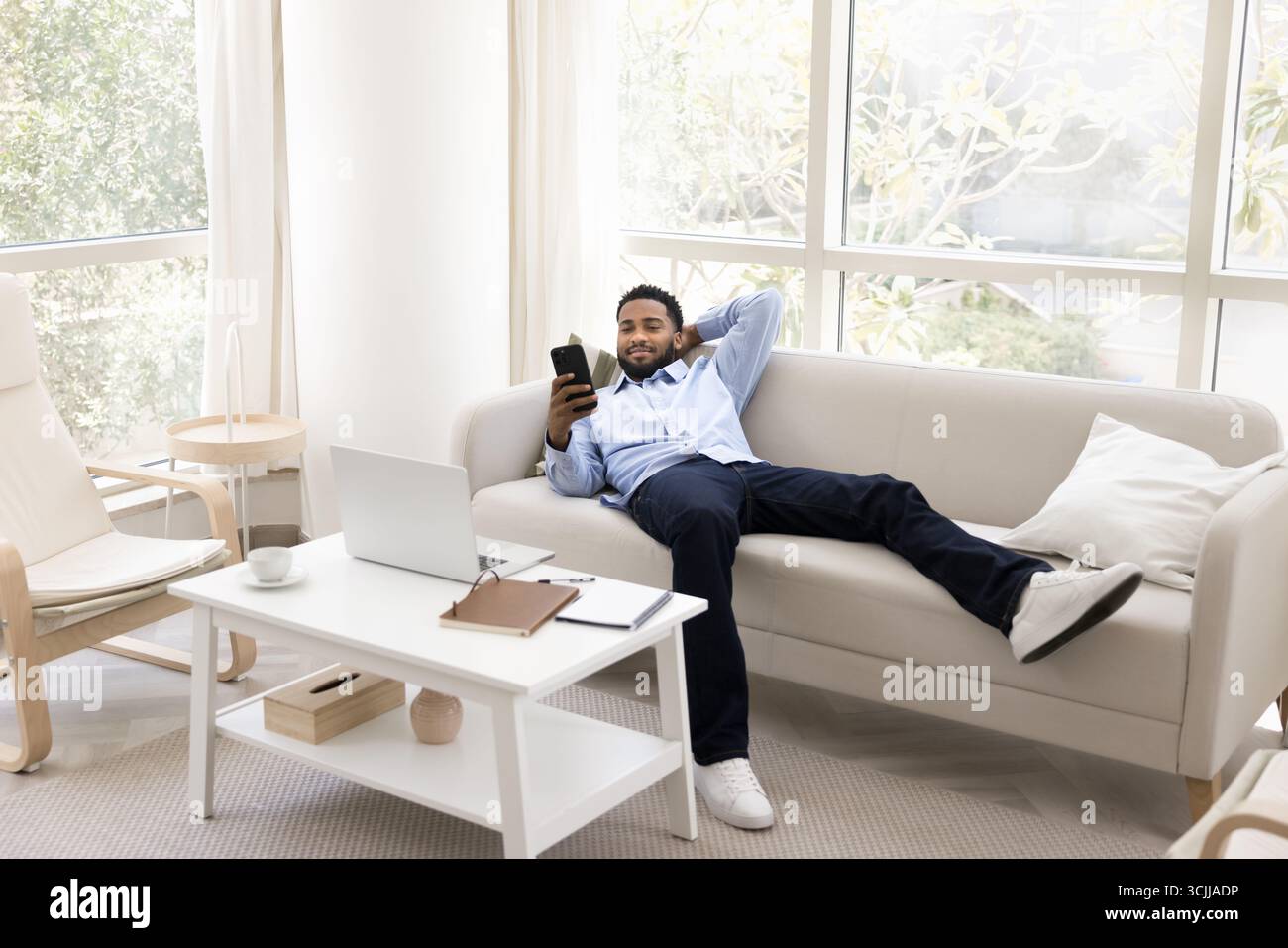 Relaxed smiling young man recline on comfy sofa using phone Stock Photo