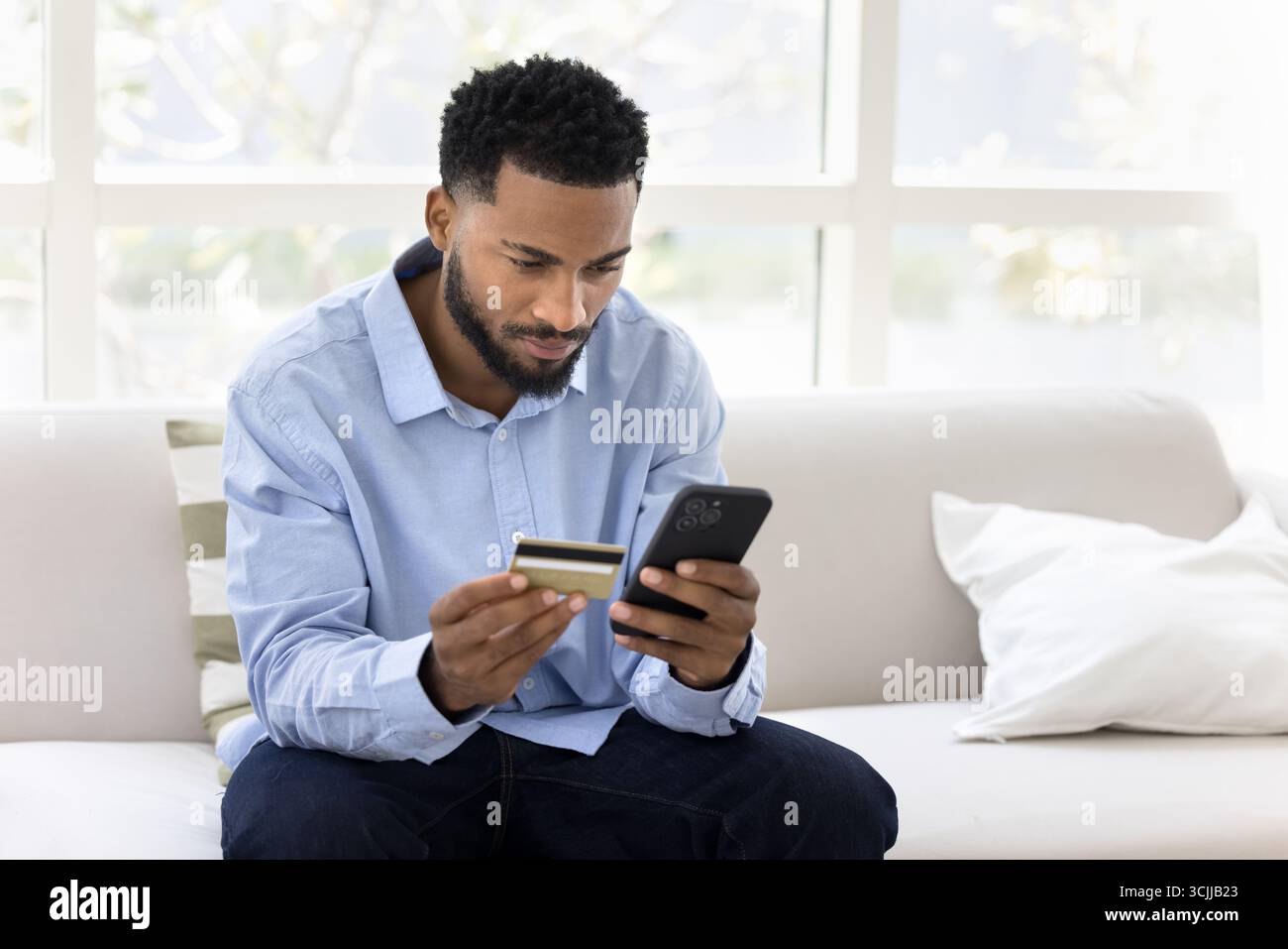 Young male using smartphone and credit card verifying online purchase Stock Photo