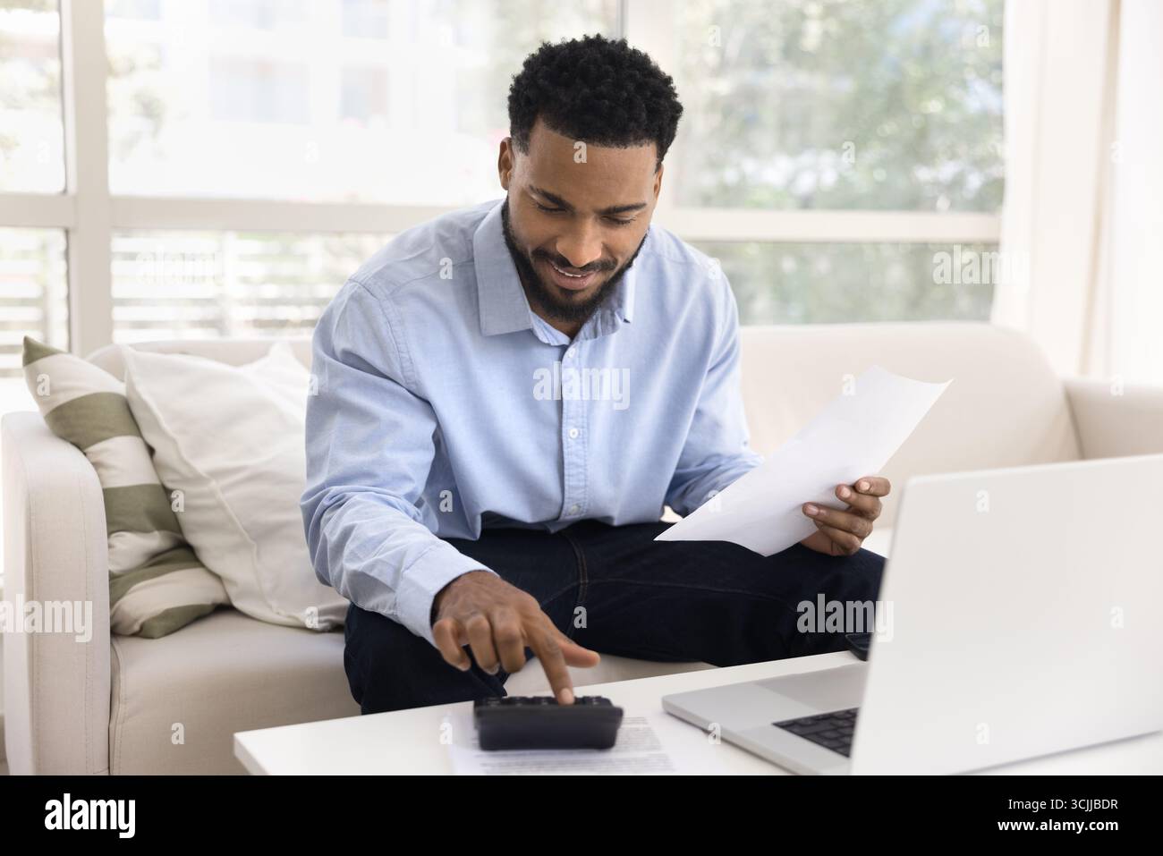 Busy smiling young man using calculator to do budgeting work Stock Photo