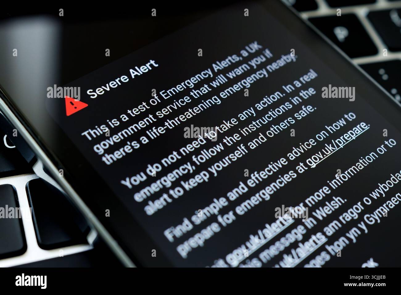 Emergency Alerts test screen on smartphone beside laptop keyboard, detailed text view. Stafford, United Kingdom, September 7, 2025 Stock Photo