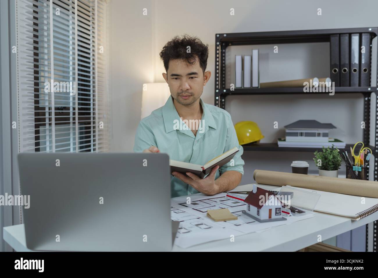Architect working on house design project using a laptop, holding a ...