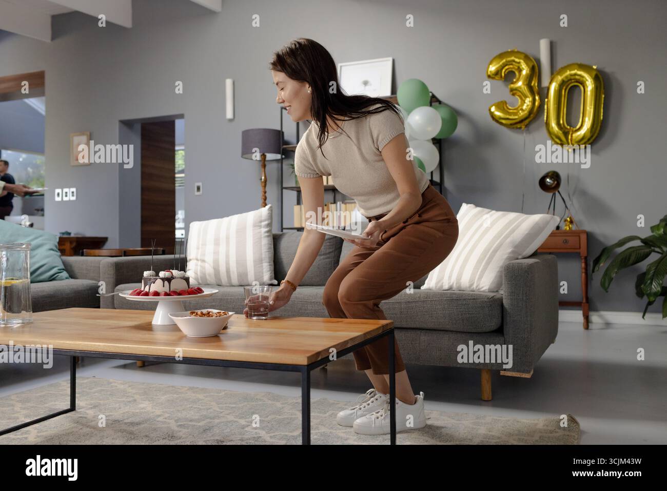 Woman preparing table with cake and snacks for birthday celebration at ...