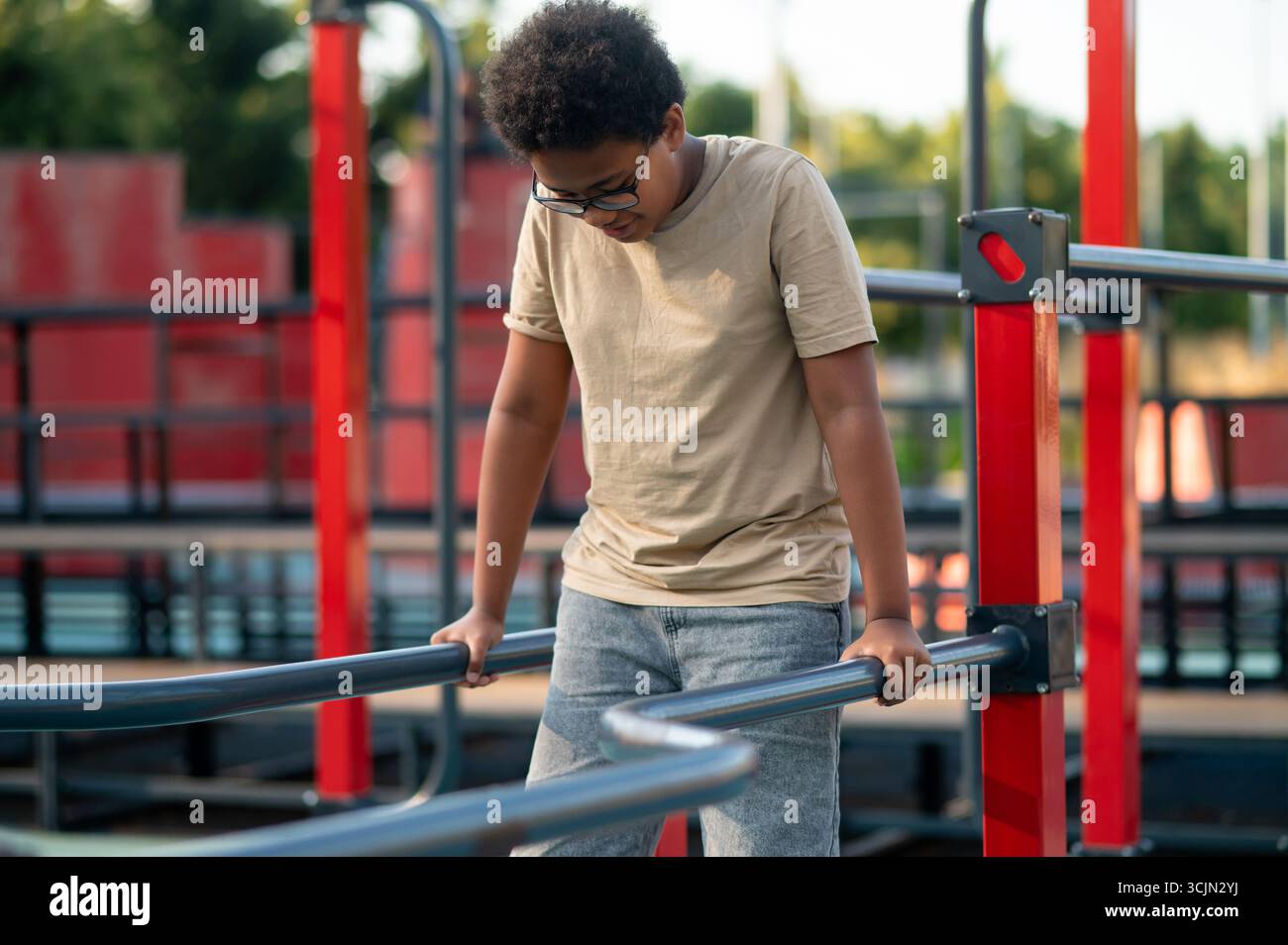 Curly-haired boy in eyeglasses spending time at the playground Stock Photo