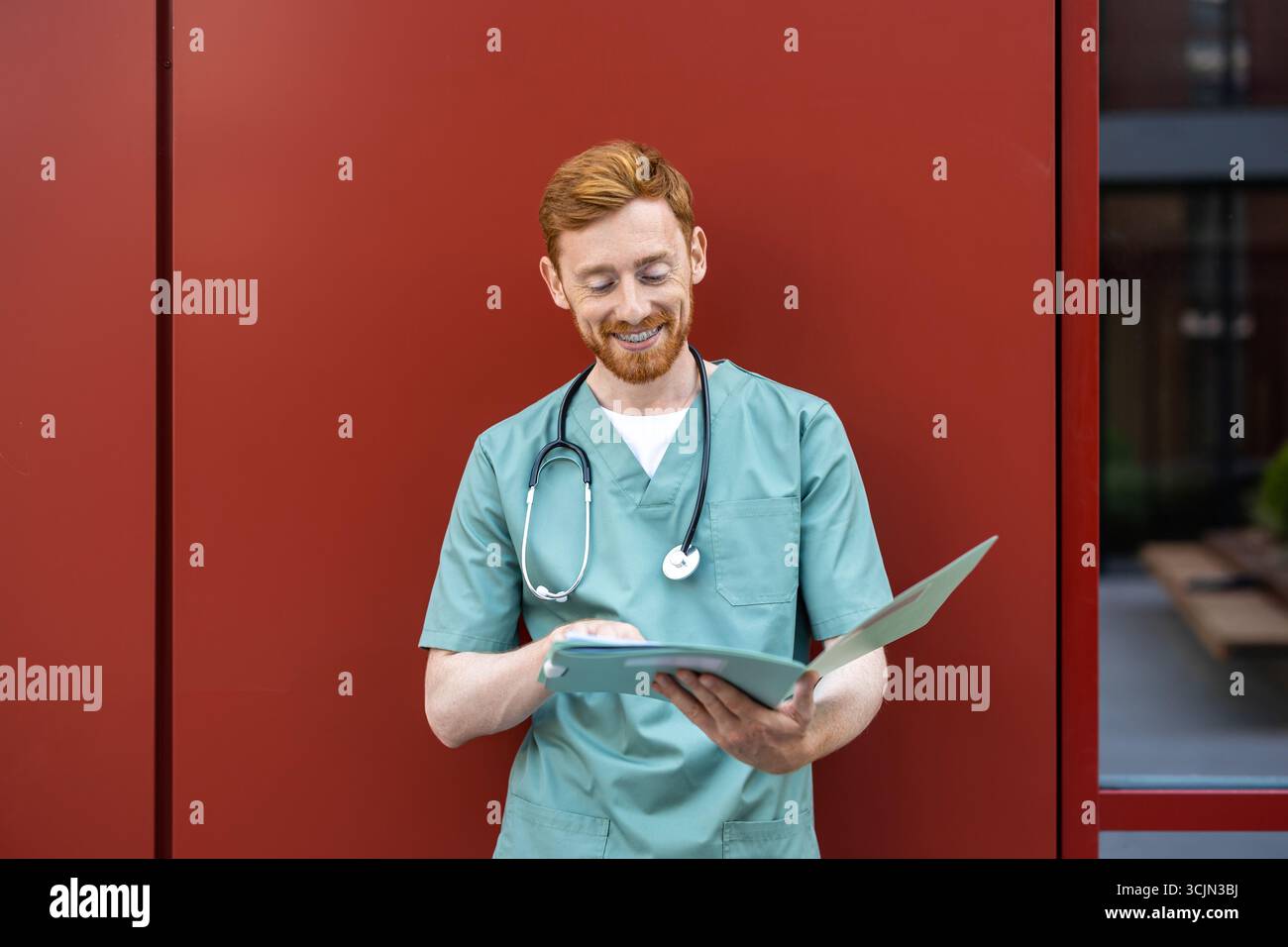 Man doctor holding open paper folder while leaning on wall Stock Photo