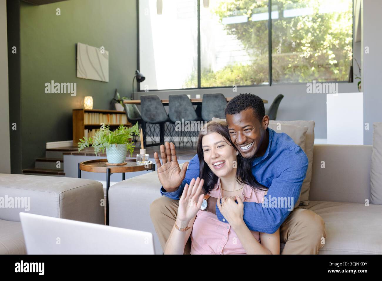 Couple video chatting on laptop at home, smiling and waving happily Stock Photo