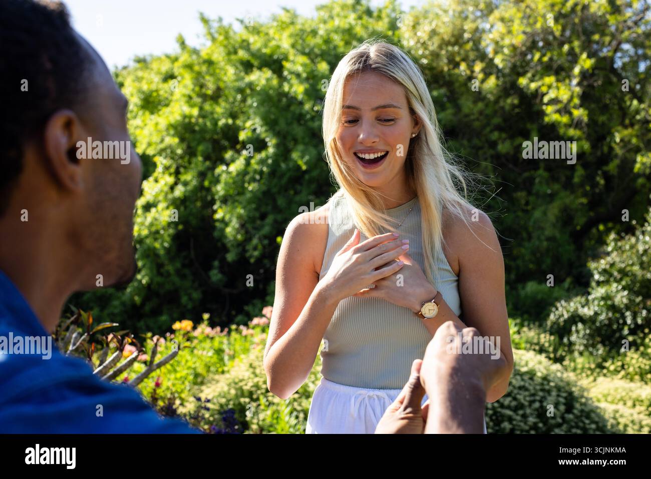 Man proposing to surprised woman in garden, both smiling with joy Stock Photo