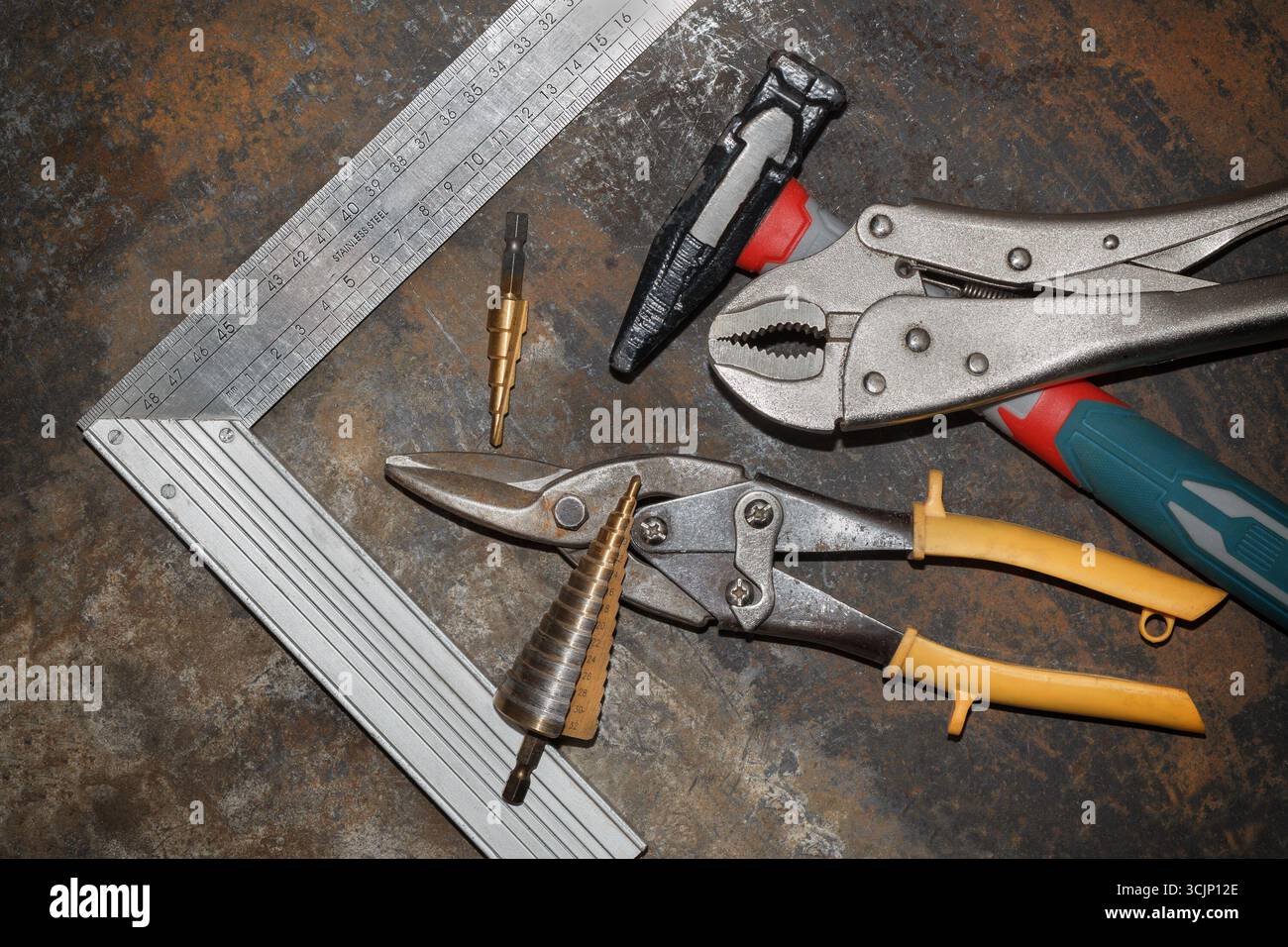 Hammer, metal shears, step drill bits, square and clamp on rusty metal workbench Stock Photo