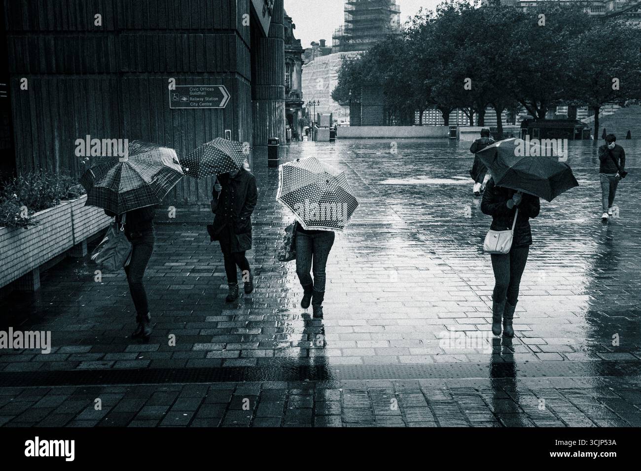 Four women with umbrellas head down against the wind and  rain in city. Stock Photo