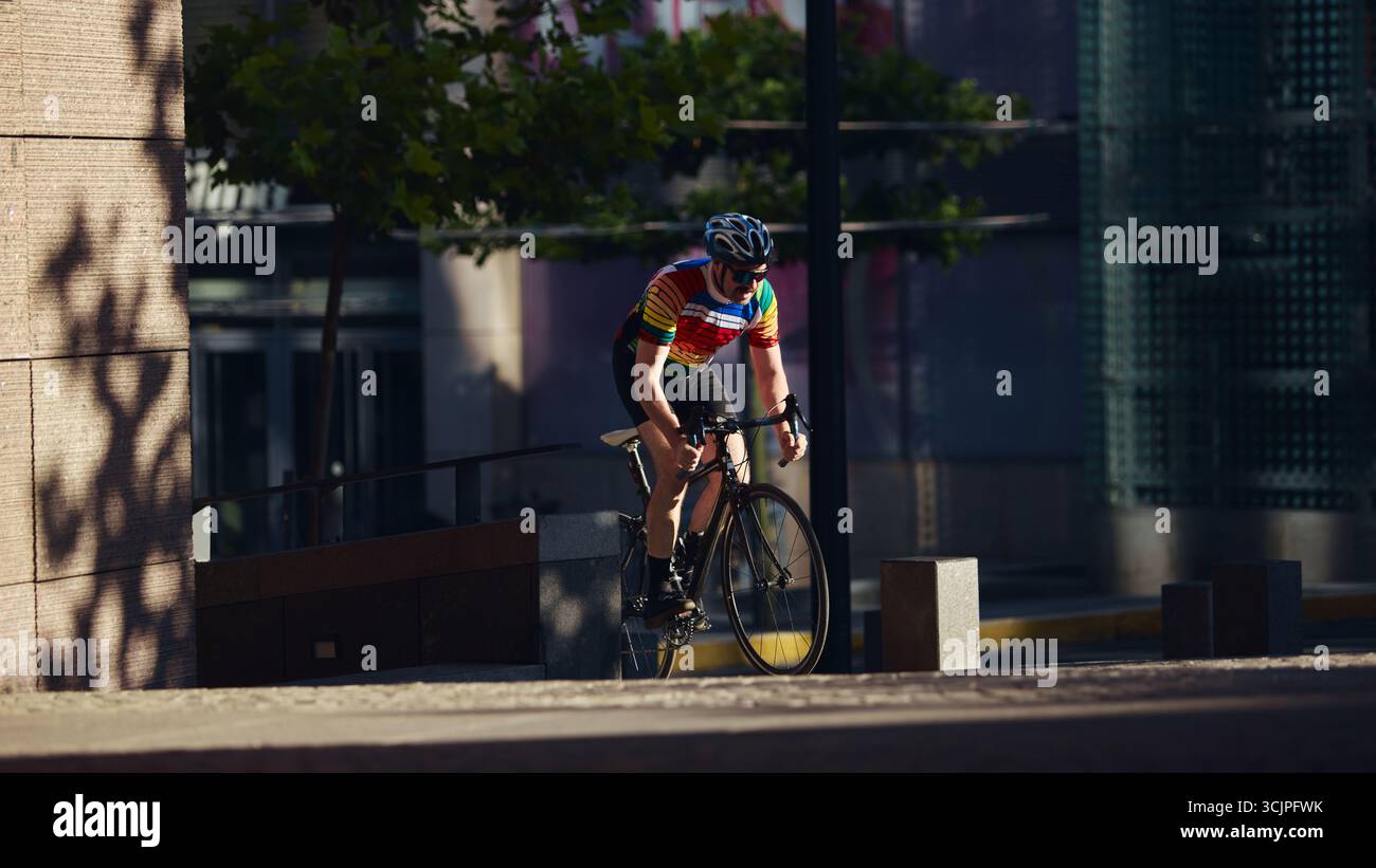 Bike Riding In Roard Cyclist in rainbow jersey riding road bike in shaded urban street with ...