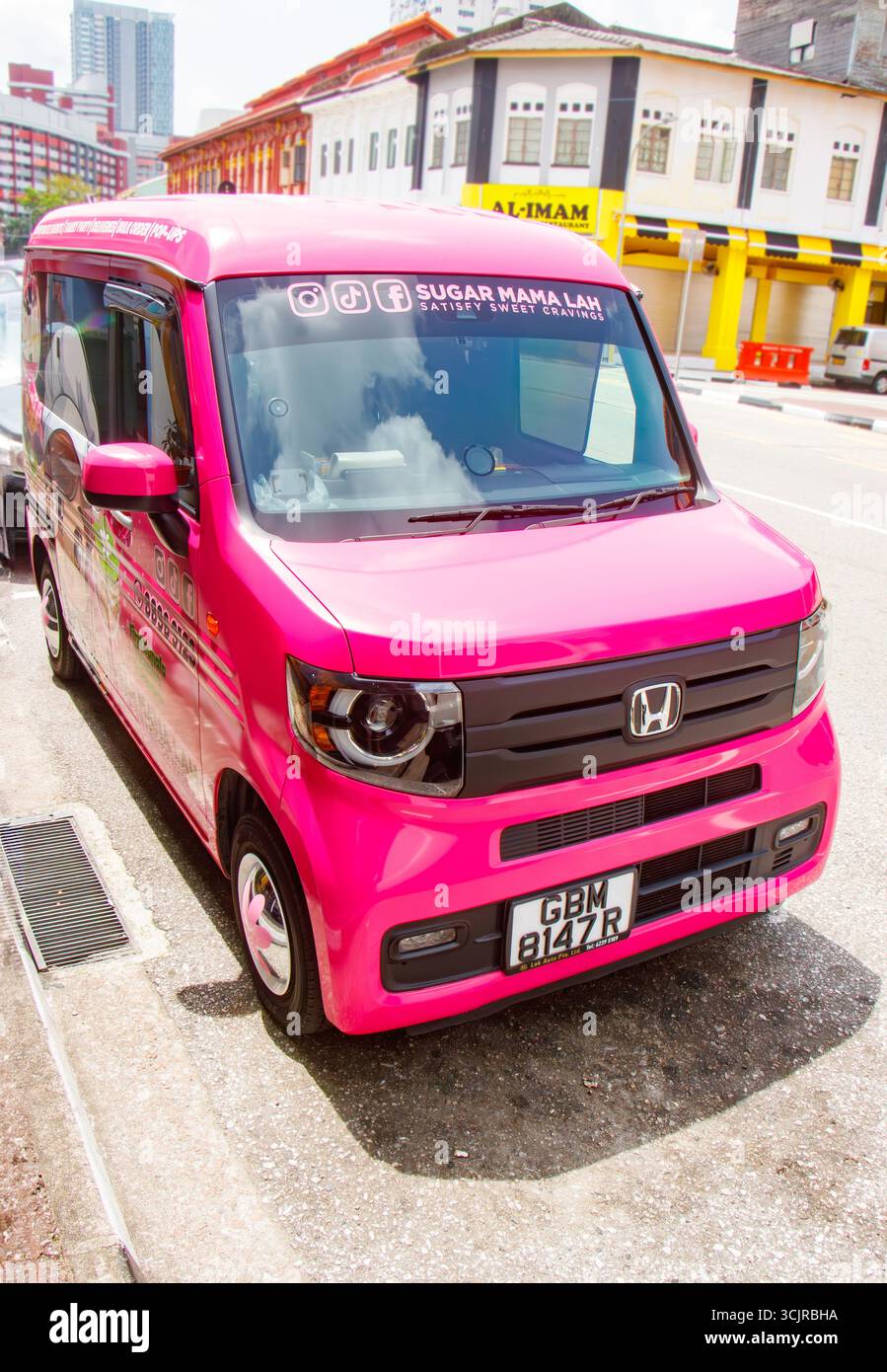 Bright pink Honda delivery van parked on street with colourful, traditional shophouses buildings in the background under a sunny sky in singapore asia Stock Photo