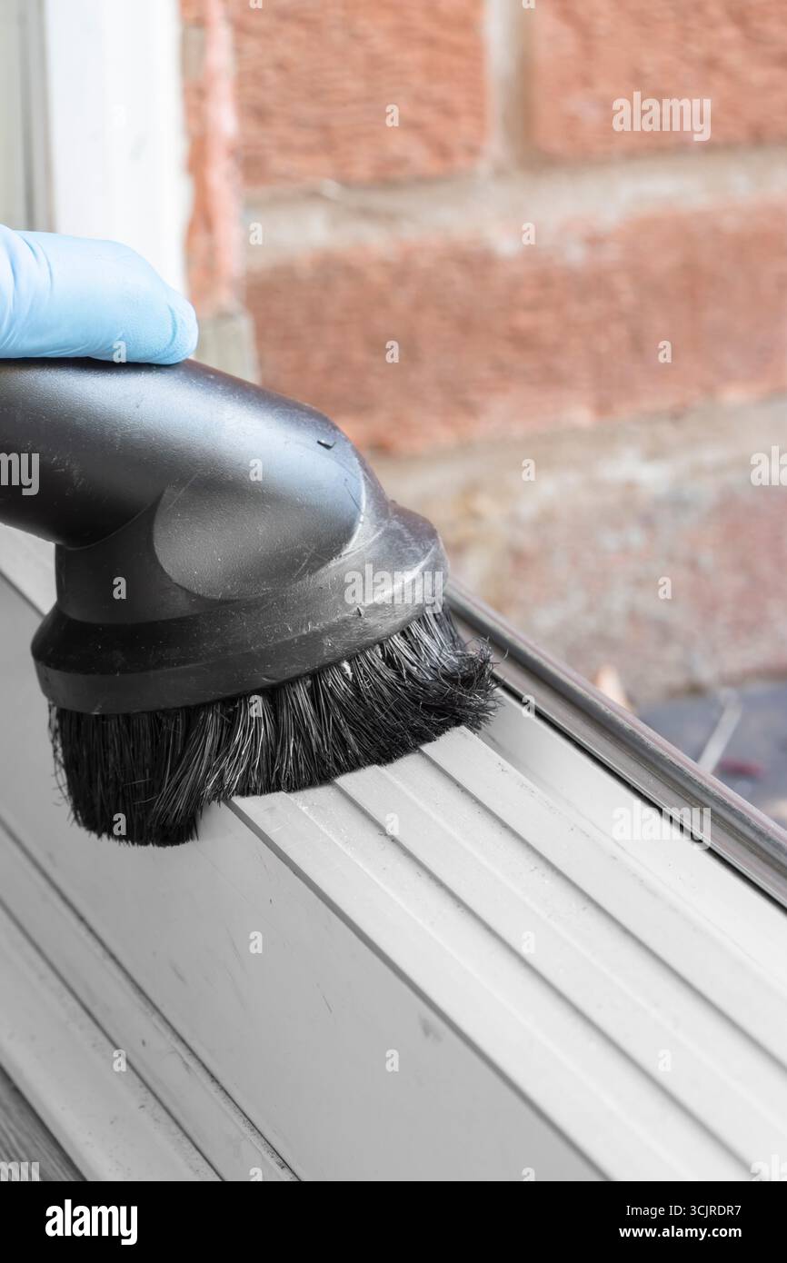 Person hoovering the threshold on a PVC sliding patio door with a brush attachment. Household chore concept Stock Photo