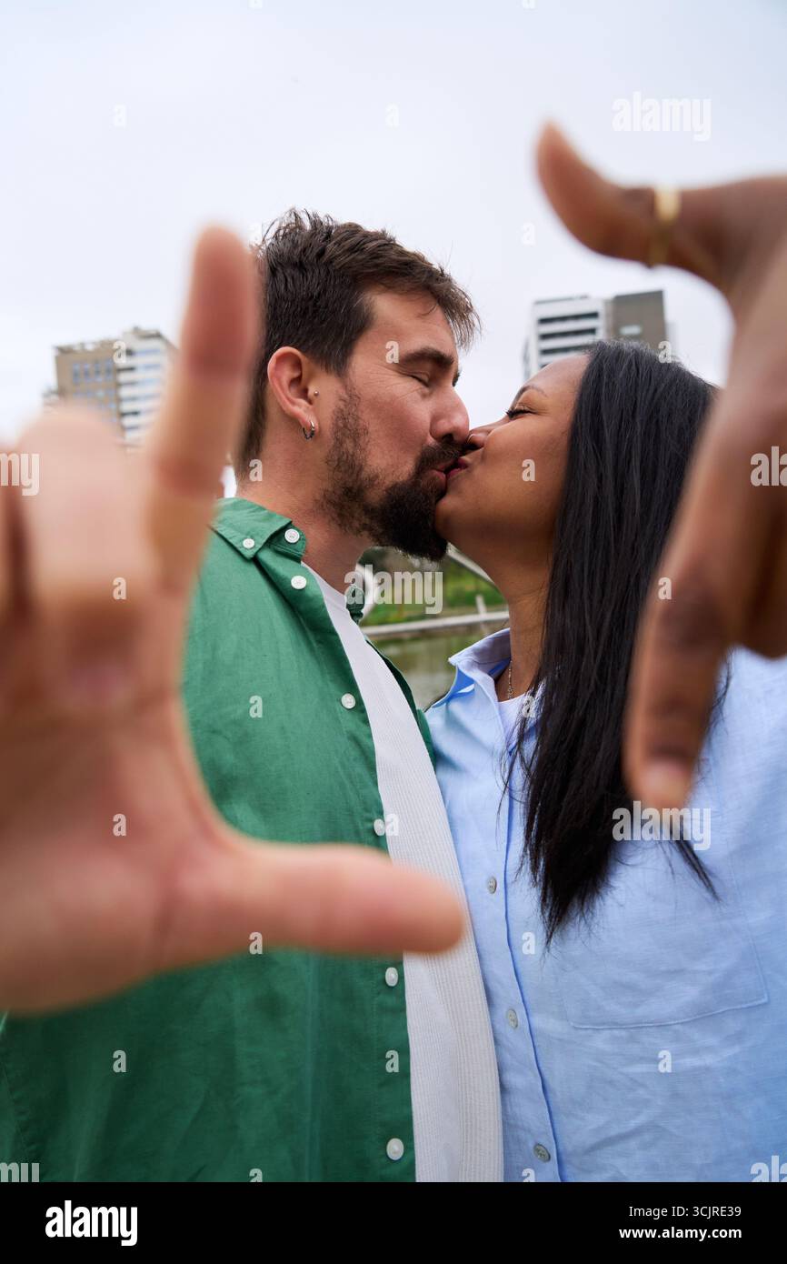 Happy multiracial couple taking a photo framing with hands in a city park Stock Photo