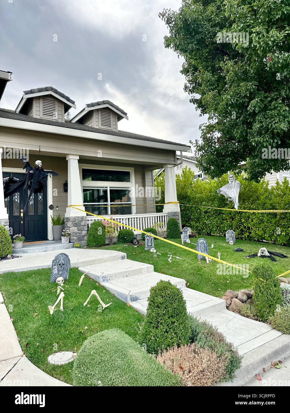 Suburban house front yard transformed into a Halloween scene with skeletons, gravestones, caution tape, and ghost decorations. Stock Photo